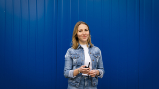 Die Mitarbeiterin steht vor einer blauen Containerwand mit einem Walkie-Talkie in der Hand.