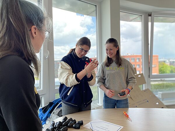 Zwei Mädchen schauen mit Elektrikerin Celine Schröder eine Zange genauer an. 