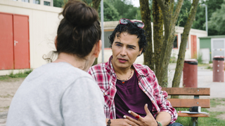 2 Menschen sprechen miteinander auf einer Bank.