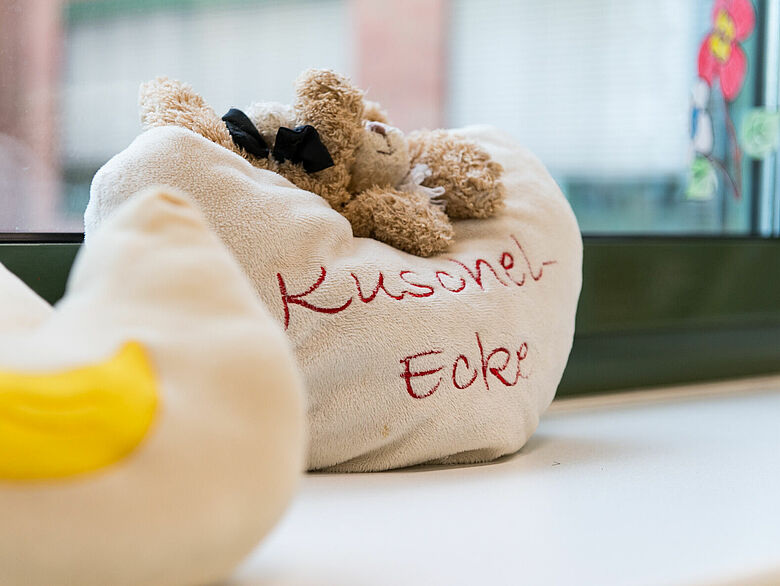 Ein Teddy auf einem Kissen beschriftet mit dem Wort "Kuschelecke".