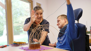 Zwei Menschen flechten einen Korb.