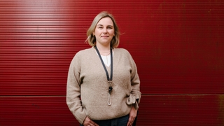 Annalena steht vor einer dunkelroten Containerwand und lächelt in die Kamera