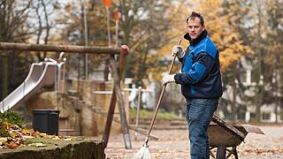 Ein Mann fegt Laub auf einem Spielplatz.