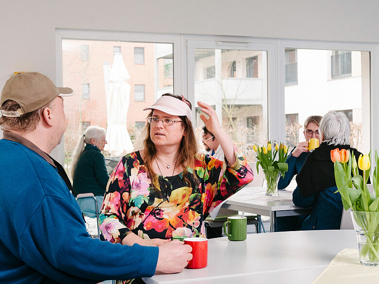 Begegnung im offenen Treffpunkt: Mehrere Personen sitzen mit Kaffeetassen an Tischen und unterhalten sich.