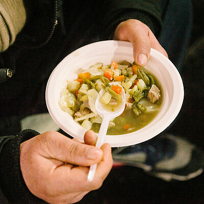 Suppe in zwei Händen eines Obdachlosen