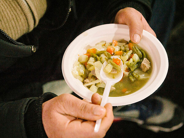 Nahaufnahme gefüllter Suppenteller mit Löffel in den Händen einer Person