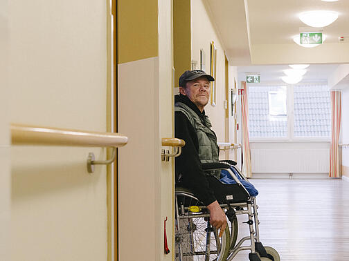 Ein Mann mit Rollstuhl schaut aus einer Tür