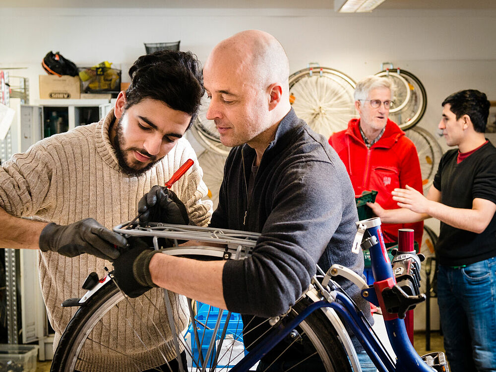 Freiwilliger Helfer und Geflüchteter reparieren Fahrräder