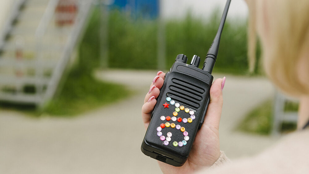 Ein Walkie-Talkie mit zwei Buchstaben aus aufgeklebten Straßsteinen.