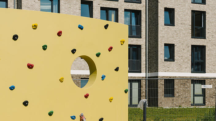 Eine Kletterwand vor einem Neubauhaus.