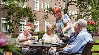 Mehrere ältere Personen trinken Kaffee in einem Garten