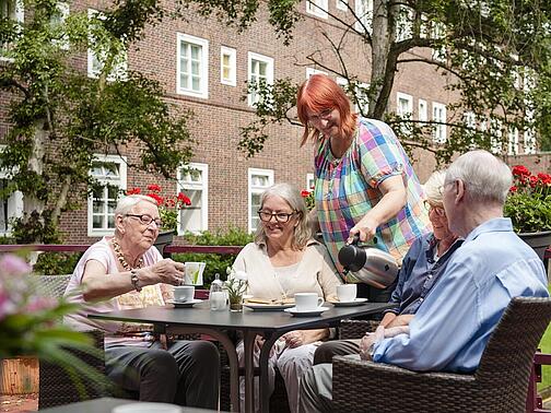 Mehrere ältere Personen trinken Kaffee in einem Garten